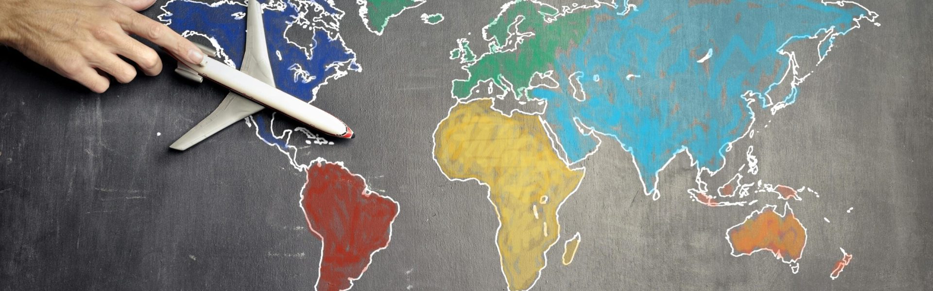 pexels-photo-3769138-3769138 Top view of crop anonymous person holding toy airplane on colorful world map drawn on chalkboard